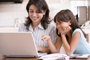 woman and young girl in kitchen with laptop and paperwork smiling