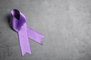 Purple ribbon on grey stone background, space for text. Domestic violence awareness
